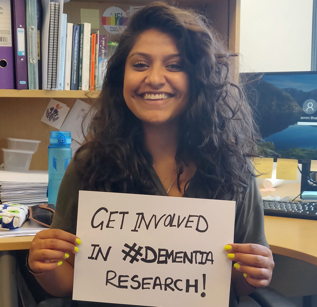 PHD student Jem Bhatt holds up a sign reading "Get involved in dementia research"