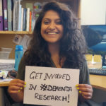 PHD student Jem Bhatt holds up a sign reading "Get involved in #dementia research"