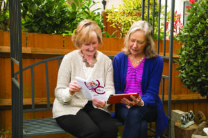 Two women sat on a bench together reading a leaflet about Join Dementia Research