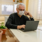 Man wearing facemask using laptop and phone